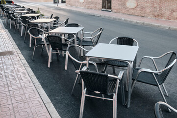 Black and white metal tables and chairs near a street cafe.Rows of empty aluminium tables and chairs cleaned and ready for the  opening time of a cafe.