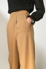 Female model wearing beige smart casual high rise wide trousers. Studio shot.	