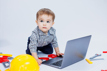 Fototapeta na wymiar A cute little boy in a checkered shirt sits on a white background with a laptop. Children's toys