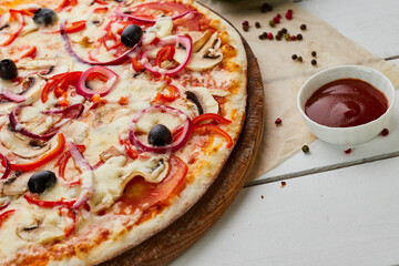 Freshly baked Vegetarian pizza with Tomatoes, mushrooms, red pepper, olives, onion and Mozzarella served on wooden background with sauces and herbs. Food delivery concept. Restaurant menu