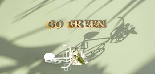 Go green text with bycicle on green background with hard shadows. Sustainable lifestyle concept