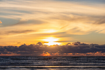 Picturesque sunset in the sea. Reflection of sunlight in the sea, clouds like a mountain range above the horizon and the sun above the clouds in the background. Copy space. Background for quotes.