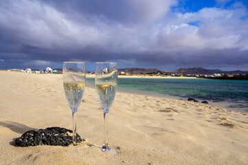 Two glasses of white champagne or cava sparkling wine served on white sandy tropical beach and blue ocean, romantic vacation, winter sun on Fuerteventura, Canary, Spain