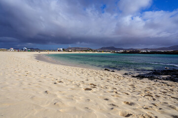 White sand, blue water and stormy clouds on La Concha beach, El Cotillo surfers village, Fuerteventura, Canary islands, Spain