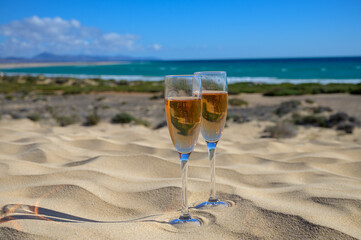 Two glasses of rose champagne or cava sparkling wine served on white sandy tropical beach with dunes and blue ocean, romantic vacation, winter sun on Fuerteventura, Canary, Spain