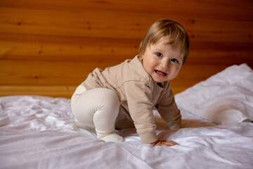 Fototapeta premium A baby is crawling on a bed with a wooden wall behind him.