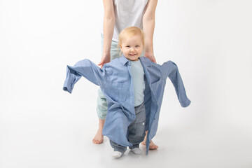 Unrecognizable young woman mother holding hands of wonderful little blond girl baby daughter wear oversized denim shirt.