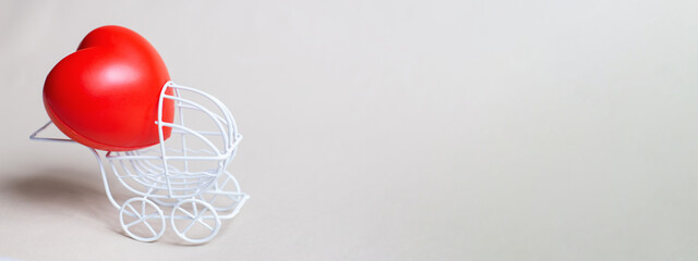 Red heart in the pram or carriage isolated on beige background.