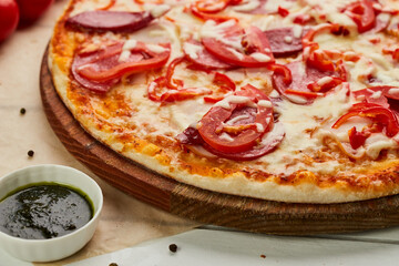 Freshly baked pizza with smoked sausages, red pepper and tomatoes served on wooden background with sauce and herbs. Food delivery concept. Restaurant menu