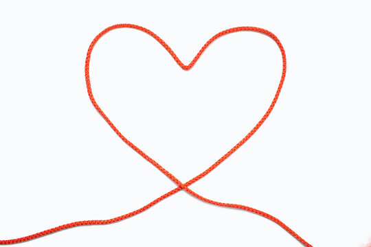 Red rope in the form of a heart on a white isolated background. The concept of love in the form of a figuratively folded red rope in the shape of a heart. Beautiful top view of a red thread heart