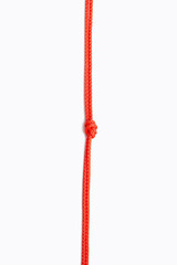 Red rope with a knot in the center on a white vertical background. Red nylon rope is arranged vertically with knots in the center