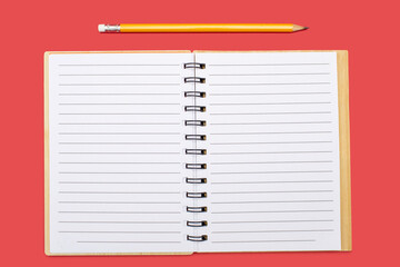 An open notebook with a binding and a yellow pencil on a red background. Open notepad with blank sheets in top view. Free space for text. Blank notebook pages ready to be used in design