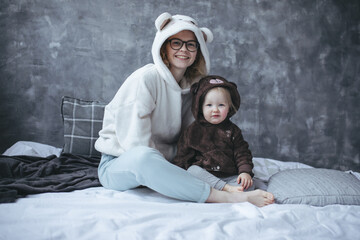 Portrait of sweet family wearing hoodies with bear heads on hoods, sitting on bed on grey marble...