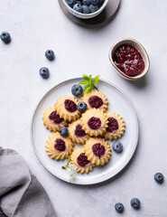 Delicious kurabye cookies with berry filling on a blue background with blueberries and jam. Healthy homemade cakes with berries.