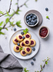 Homemade kurabye cookies with berry filling on a blue background with blueberries and jam. Healthy and delicious pastries with berries.