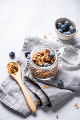 Homemade baked granola with nuts and fresh blueberry in a jar on a light background with napkin. Healthy vegetarian muesli for breakfast.