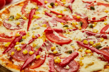 Freshly baked tasty pepperoni pizza with salami, mozzarella cheese, corn and pepper served on wooden background with tomatoes, sauce and herbs. Food delivery concept. Restaurant menu