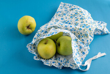 Apples in an eco-bag on a blue background. The concept of reuse, an eco-friendly approach to everyday life.