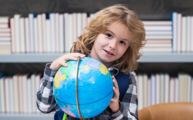 School pupil looking at globe in library at the elementary school. World globe. Kid boy from elementary school with book. Concept of education and learning.