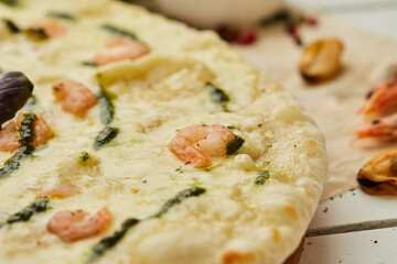Freshly baked tasty pizza with shrimps and mozzarella cheese served on wooden background with tomatoes, sauce and herbs. Food delivery concept. Restaurant menu