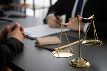 Focus shiny golden balanced scale on blurred background of lawyer colleagues working on desk at law...