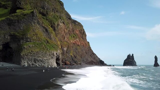 Aerial drone footage of Pointy rocks sticking out of the ocean at Reynisfjara Beach near Vik in Iceland. Pointy Rock cliffs at black sand beach. Basalt cave with basalt column. High quality 4k footage
