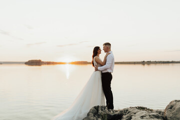 Groom and bride standing on the rocks. They hugging and looking each other, just married couple....