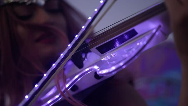 Close-up violin bow with led light in hand of blurred unrecognizable woman playing music in darkness at night. Caucasian confident talented musician performing outdoors