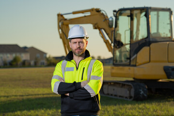 Caucasian man, construction worker in helmet at construction site. Industry engineer worker in hardhat near bulldozer or digger tractor. Concept of construction industry. Construction site manager.