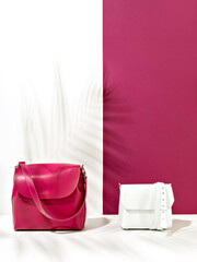 An elegant closeup of a set of two small female handbags with the background color play of saturated pink and white. The leaf shadow adds the summertime atmosphere of lightness and freshness.