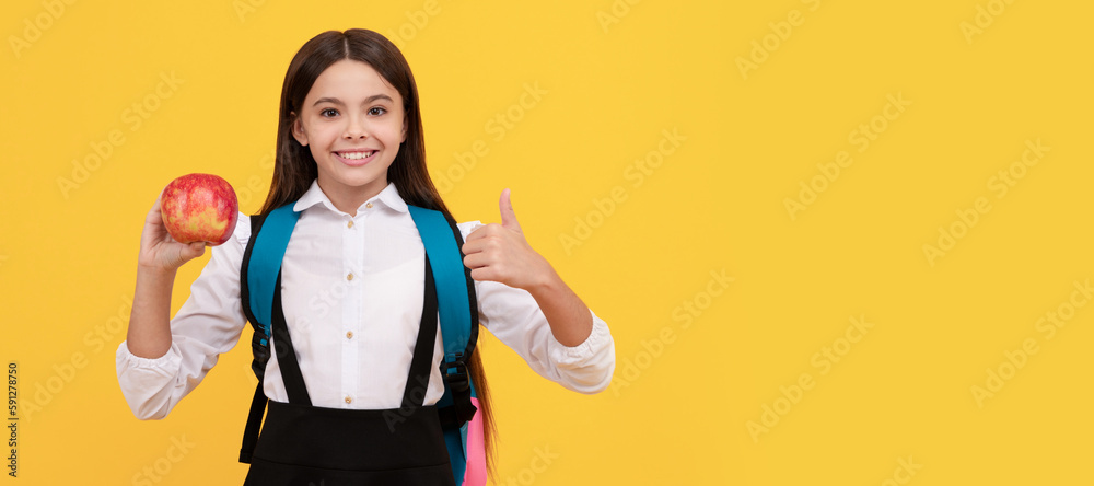 Wall mural happy girl child give thumbs up holding apple and school bag yellow background, education. banner of