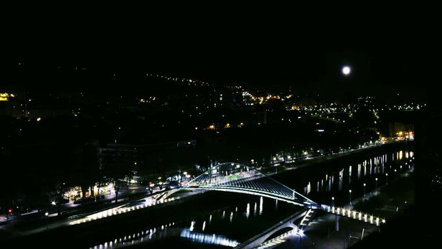 High perspective night timelapse of Zubizuri arch footbridge crossing the Nervion River in Bilbao, Spain