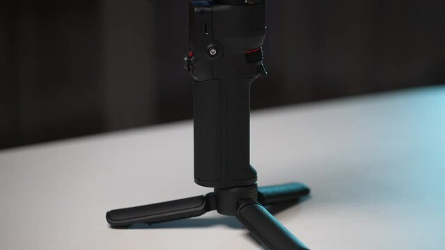 Close-up tracking shot of assembled steadicam on blurred background with bokeh lights. Stages of assembling and preparing professional modern electronic stabilizer for work. Shooting in slow motion.