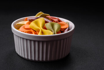 Raw farfalle pasta in different colors on a dark concrete background