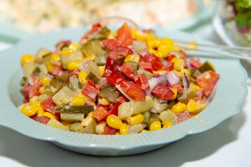 Fresh salad with red pepper, yellow corn, green salted cucumber, onions and tomato pieces on white plate staying on kitchen table. Healthy food and diet concept. Vegetarian food. Selective focus