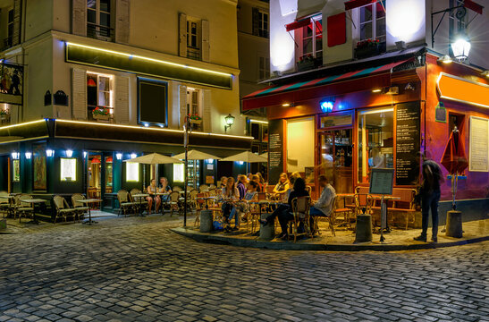 Typical night view of cozy street with tables of cafe and easels of street painters in quarter Montmartre in Paris, France