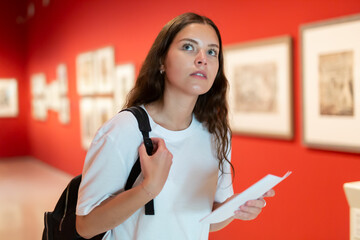 Portrait of a young girl visitor with a paper guide at the exhibition of paintings in the museum..