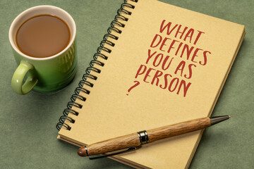 What defines you as a person? Inspirational question in a spiral sketchbook with a cup of coffee, identity and personal development concept.