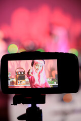 Smiling artist playing electronic song at mixer console while recording music session using professional camera, preparing to perform in night club. Dj with pink hair filming video with her performing