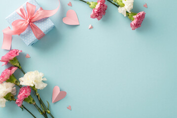 Mother's Day floral concept. Top view flat lay photo of beautiful present boxes with pink ribbons, carnation flowers, and pink paper hearts on pastel blue background with empty space