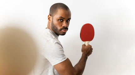 An adult dark-skinned man posing against a white background with a ping pong racket waiting to receive the ball. Ping pong player concept.