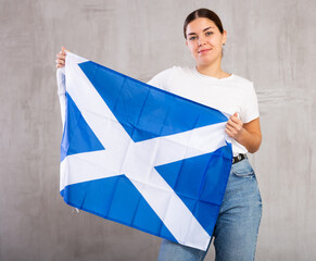 Young positive woman holding national flag of Scotland in her hands