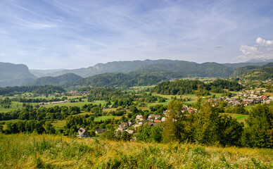 Fototapeta na wymiar A view of green pastures, a nice village and the Julian Alps in Slovenia. Beautiful day for hiking.