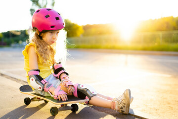 a little resentful sad girl in a pink helmet sits on a skateboard, sunset in the background and a place for text