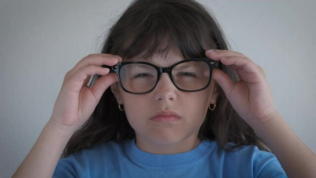 Child eyewear for vision indoor. A view of tired little girl suffering from problems with vision use glasses in the room.