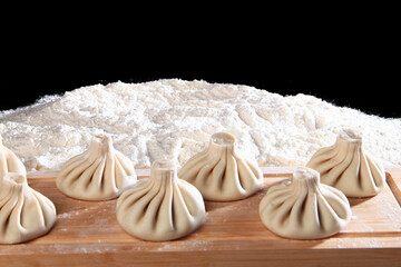 Preparation of khinkali. Khinkali are lying on the table with a mound of flour. Khinkali is formed manually before cooking. Before cooking, roll Georgian khinkali in flour. Selective focus.