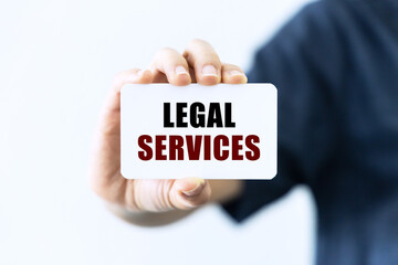 Legal services text on blank business card being held by a woman's hand with blurred background. Business concept about legal services.