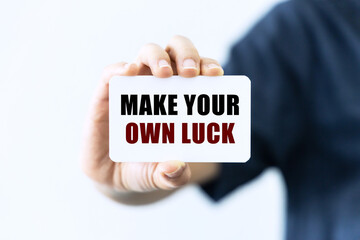 Make your own luck text on blank business card being held by a woman's hand with blurred background. Business concept about luck.