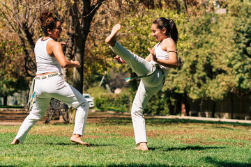 mujeres practicando patadas, ejercicios y capoeira en la ciudad con su ropa de capoeira en un...