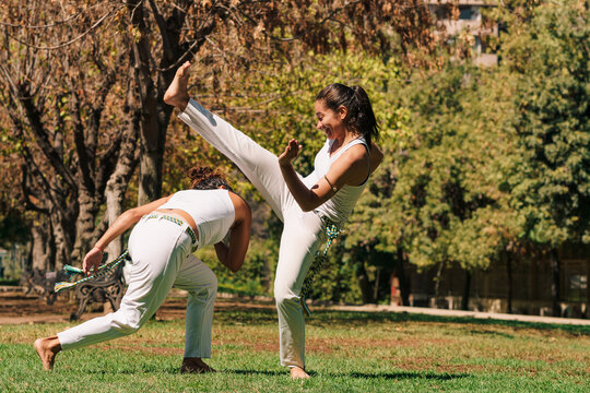 mujeres practicando patadas, ejercicios y capoeira en la ciudad con su ropa de capoeira en un parque verde en un d&iacute;a soleado.